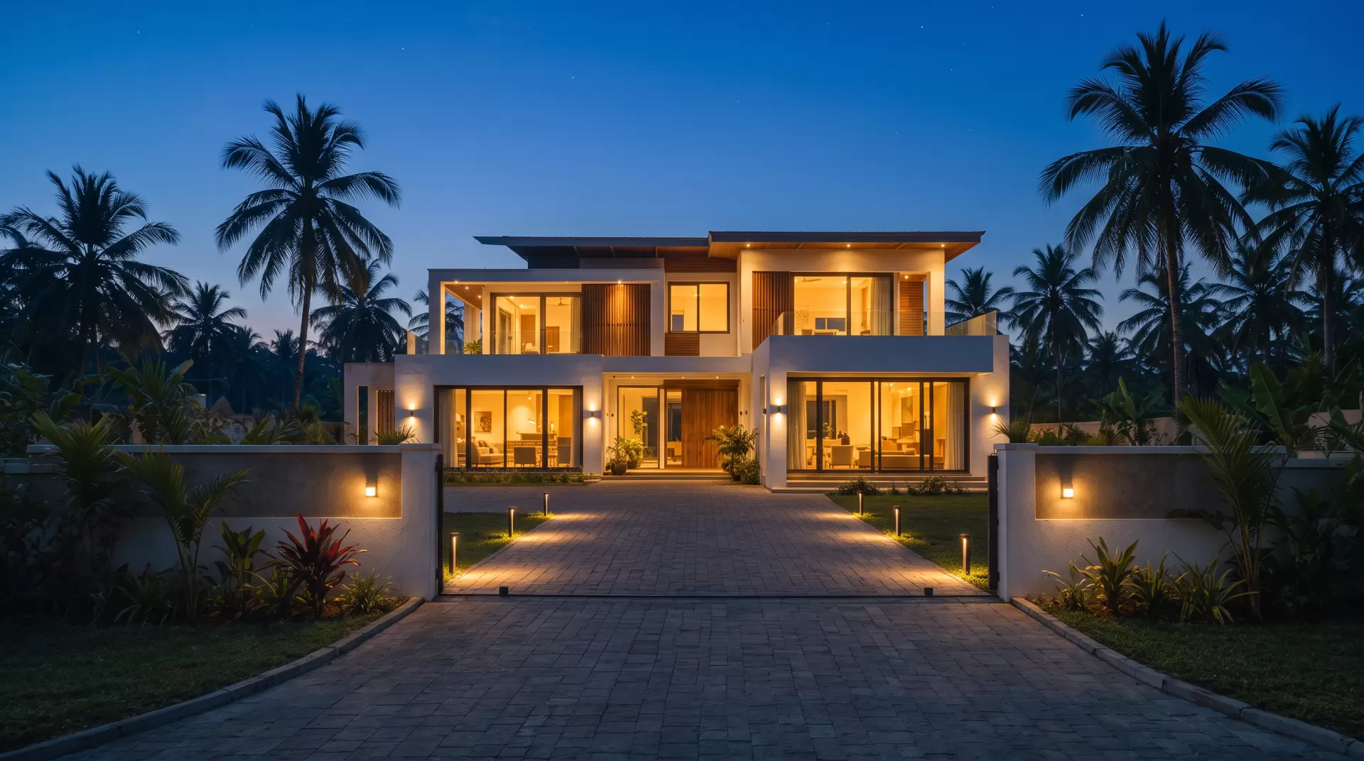 The same villa at blue hour with most windows lit and the gate open